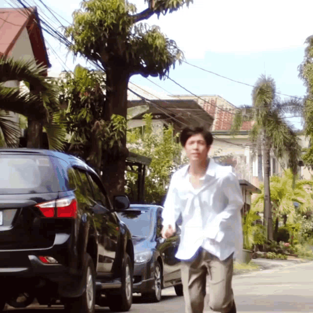 a man in a white shirt is running down a street with cars parked behind him
