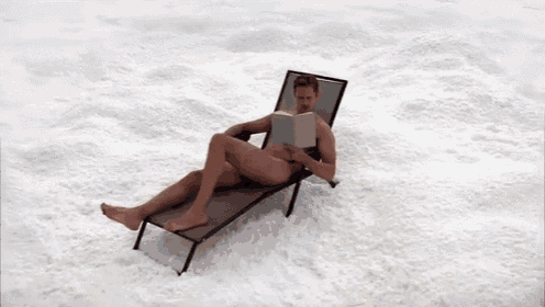a naked man is reading a book while laying on a lounge chair in the snow .