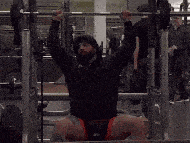 a man with a beard is squatting with a barbell in a gym
