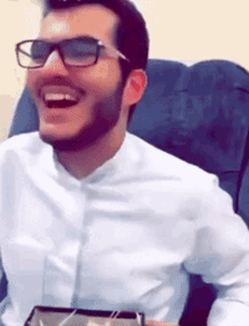 a man with glasses and a beard is laughing while sitting in a chair .