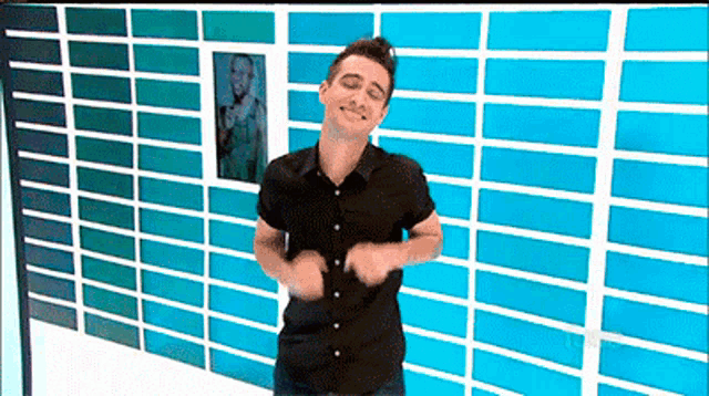 a man in a black shirt is dancing in front of a wall of blue blocks