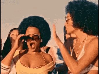 a woman with an afro and sunglasses is giving a high five to another woman in a bikini .