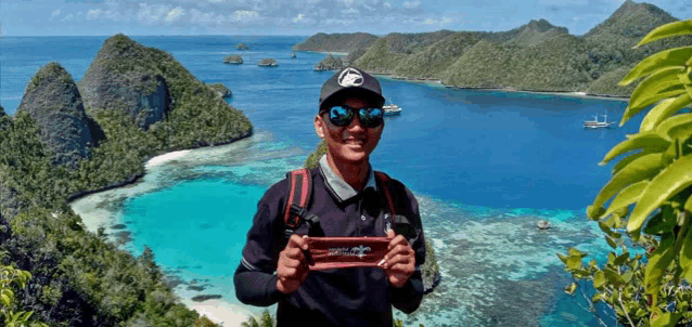 a man wearing sunglasses and a hat is standing in front of a body of water and mountains