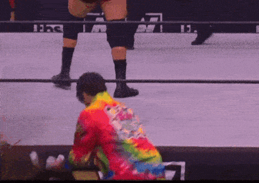 a man in a tie dye shirt is kneeling on a wrestling mat
