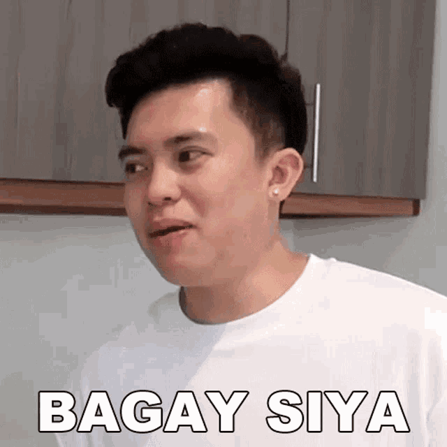 a man in a white shirt is making a funny face while standing in front of a kitchen .