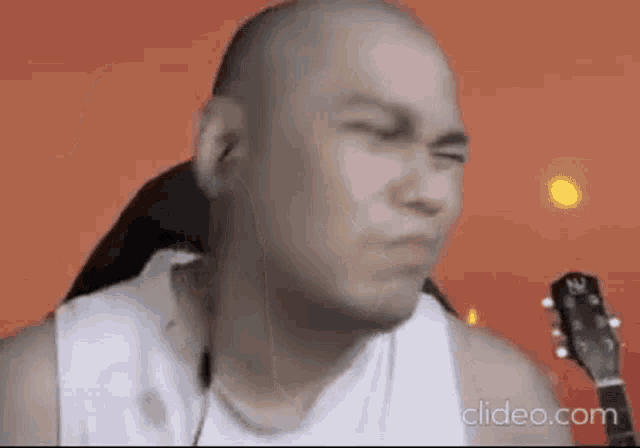 a bald man in a white tank top is playing a guitar .