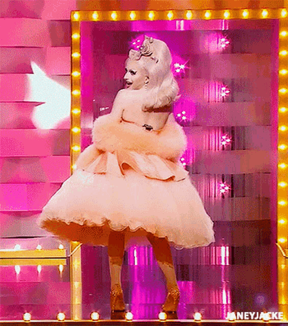 a woman in a pink dress is standing in front of a mirror on a stage .