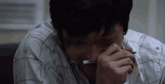 a man in a plaid shirt is covering his face with his hand while holding a pen .