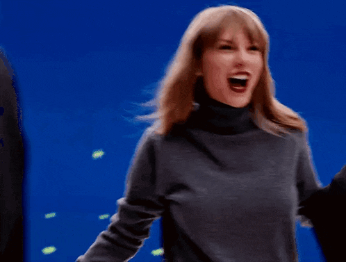 a woman wearing a grey turtleneck sweater is laughing with her mouth open