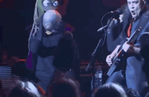 a man is playing a guitar in front of a crowd while another man holds a stuffed animal