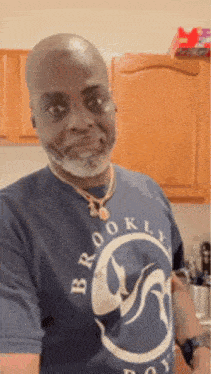 a man with a beard is wearing a blue brooklyn t-shirt and a necklace .