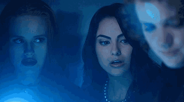 a group of women are standing in a dark room with a blue light behind them