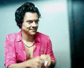 a man wearing a pink shirt and a necklace is standing in front of a mirror .