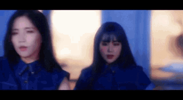 two women in blue jackets are standing next to each other in a dark room .