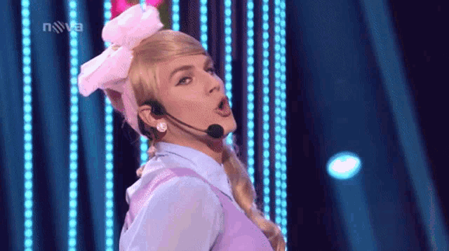 a woman with a pink bow on her head is singing into a microphone in front of a nova logo