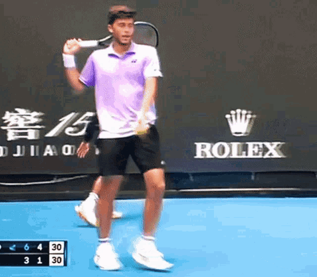 a man in a purple shirt is holding a tennis racquet on a tennis court in front of a rolex sign .