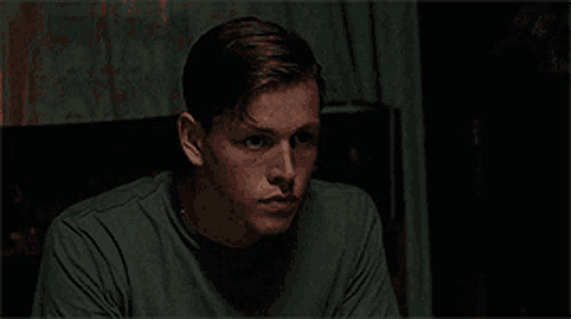 a young man is sitting on a couch in a dark room looking at the camera .
