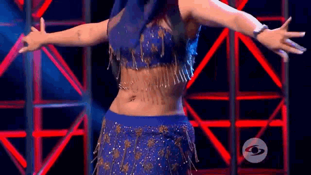 a woman in a blue top and gold skirt is dancing on a stage