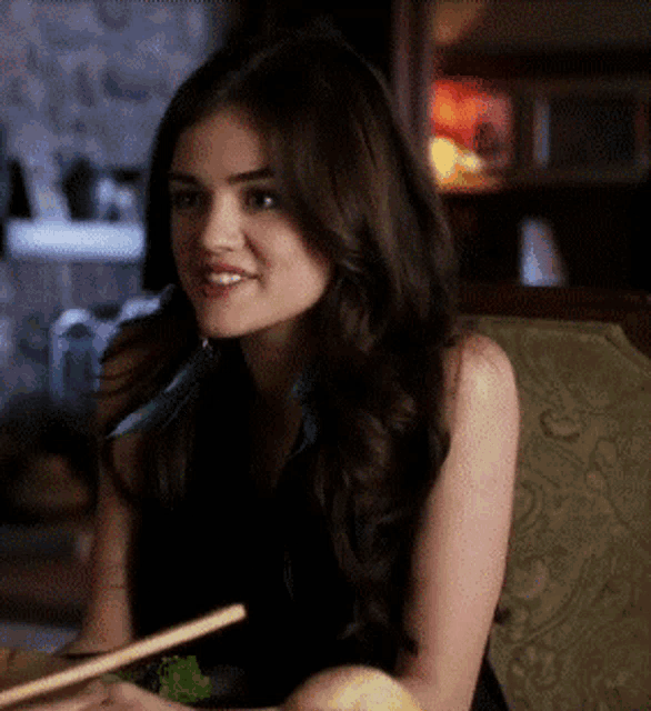 a woman is sitting at a table with chopsticks in her hand and smiling