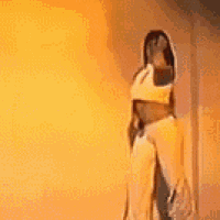 a woman is standing in front of a yellow wall and dancing .