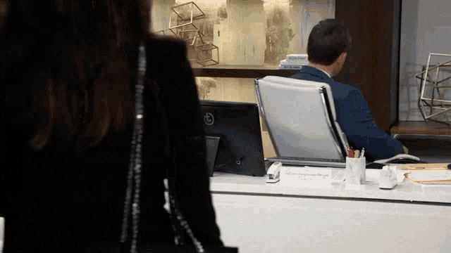 a man in a suit sits at a desk with a sign on it that says " where happiness comes from the heart "