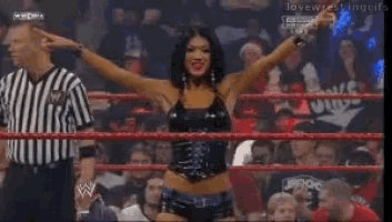a woman stands in a wrestling ring with her arms in the air