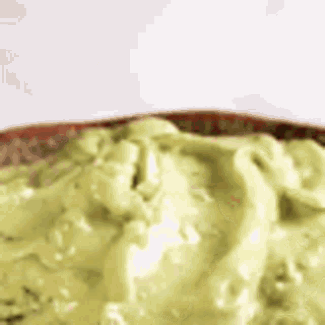 a close up of a bowl of green guacamole on a table .