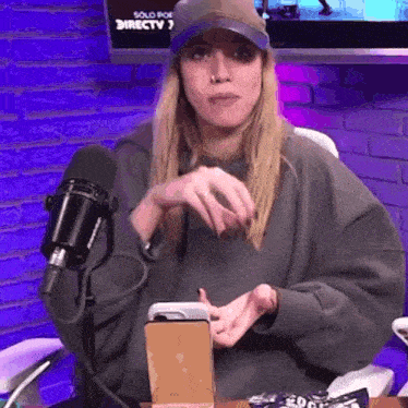 a woman wearing a hat is sitting in front of a microphone and holding a cell phone .