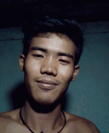 a shirtless young man with a necklace around his neck looks at the camera