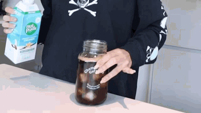 a person holding a carton of nut pods next to a jar of coffee