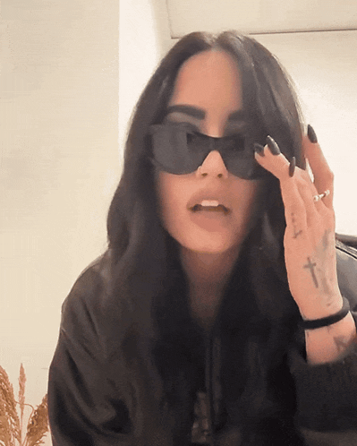 a woman wearing sunglasses has a tattoo of a cross on her left hand