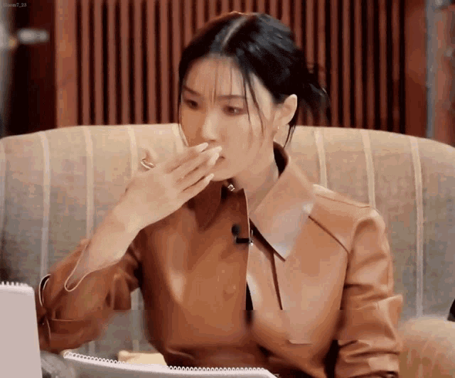 a woman in a brown leather jacket is covering her mouth