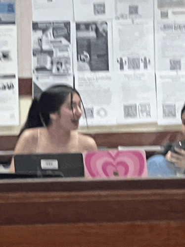 a woman sits at a desk with a pink heart shaped laptop