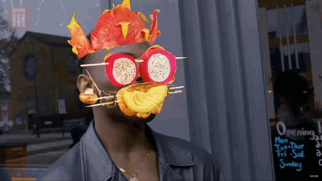 a man wearing a mask made of fruit and vegetables stands in front of a sign that says opening