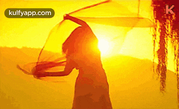 a silhouette of a woman holding a scarf in front of the sun with kulfyapp.com in the corner