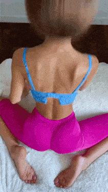 a woman in a blue bra and pink leggings is doing a split on a bed