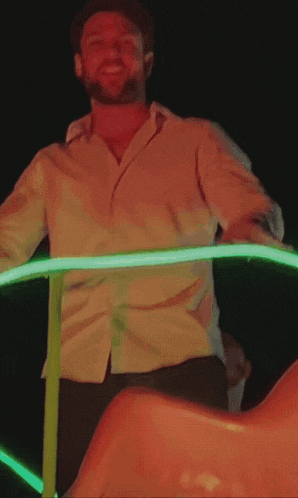 a man in a white shirt is standing in front of a neon light