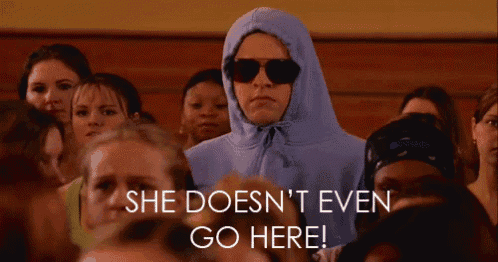 a woman wearing a hoodie and sunglasses stands in a crowd with the words she does n't even go here below her