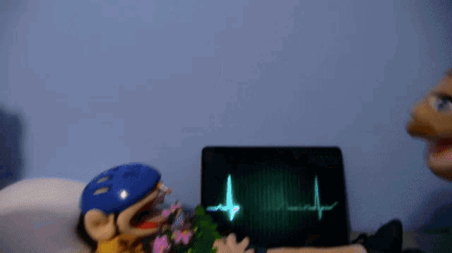 a puppet laying in a hospital bed with a heartbeat monitor behind him