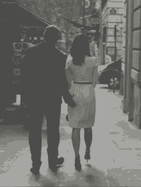 a black and white photo of a man and woman walking down a sidewalk