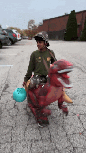 a boy in a dinosaur costume is carrying a candy bucket