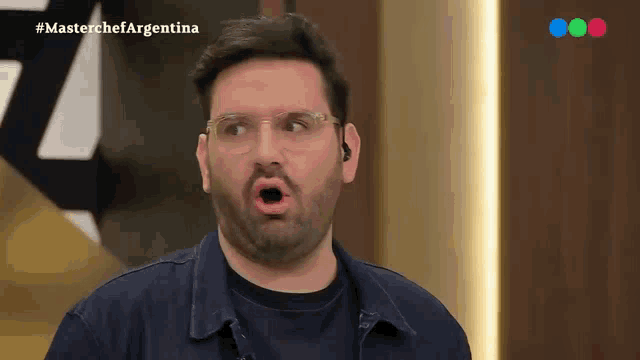 a man with glasses and a beard is making a funny face in front of a masterchef argentina sign