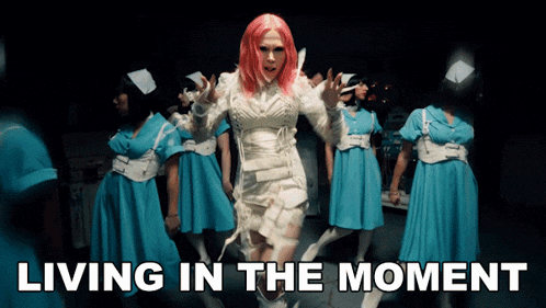 a woman with pink hair is surrounded by blue nurses and the words living in the moment