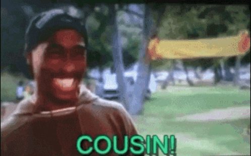 a man is laughing in a park with the word cousin written on the screen .