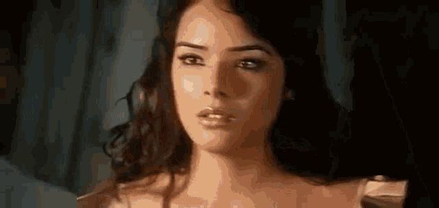a close up of a woman 's face in a dark room with a blue curtain behind her .