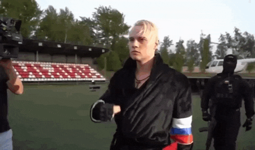 a man in a black robe with the russian flag on his sleeve is walking on a field .
