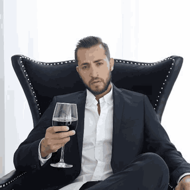 a man in a suit is sitting in a chair holding a wine glass .
