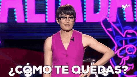 a woman in a pink dress and glasses is standing on a stage with her hands on her hips and says " como te quedas "