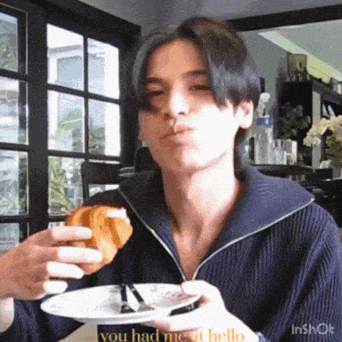 a man is sitting at a table eating a croissant and a plate of food .