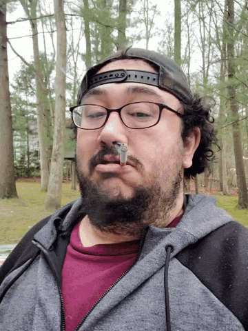 a man wearing glasses smoking a cigarette in the woods